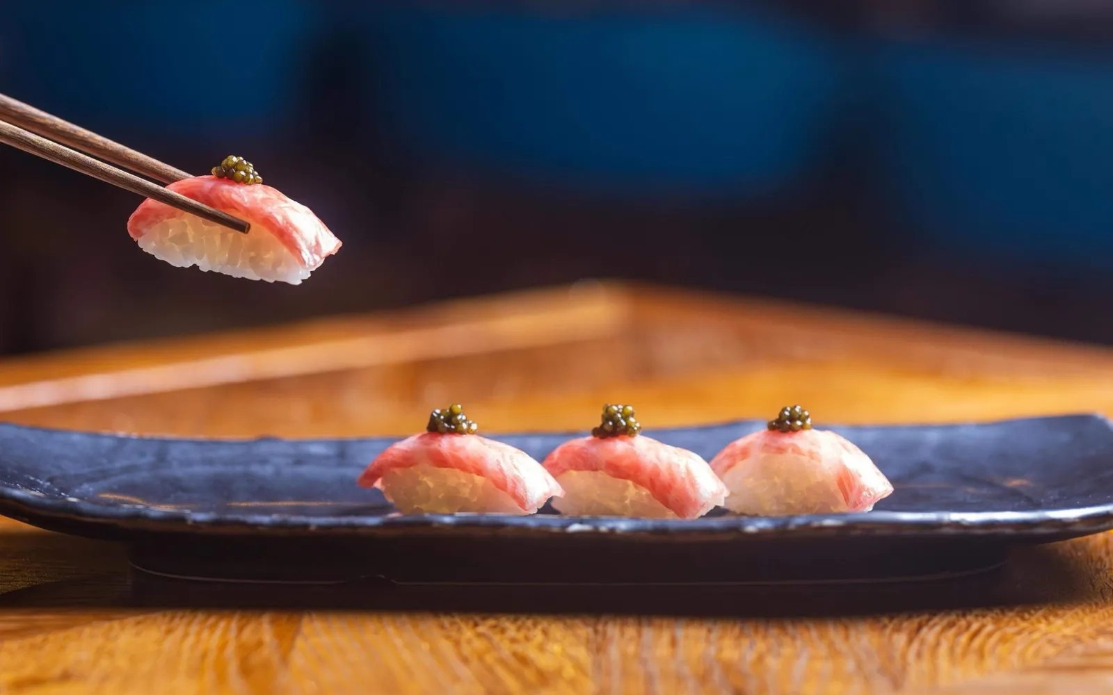 Nigiri lifted with chopsticks over a wooden counter.