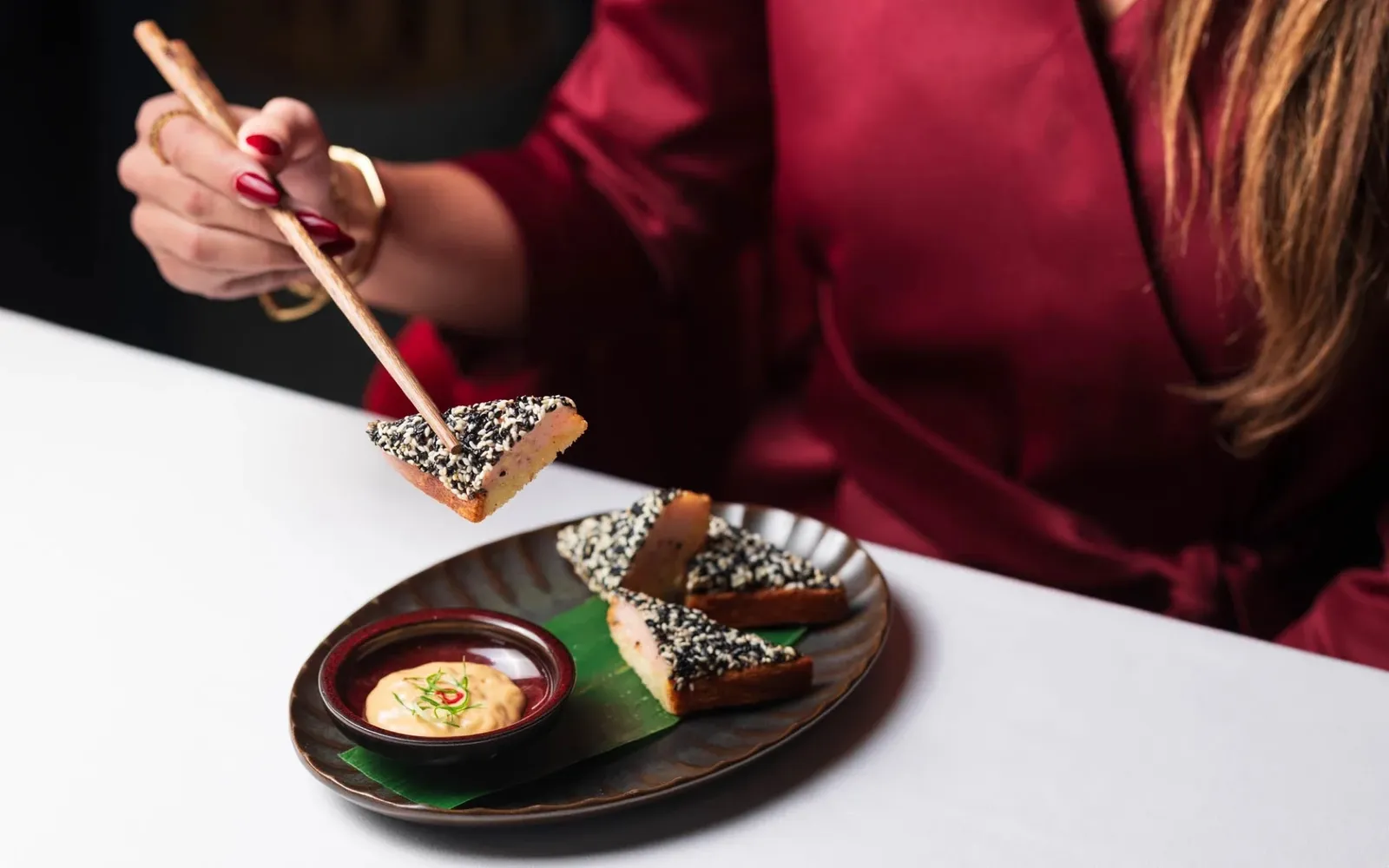 Chopsticks lifting a dessert from a dark plate.